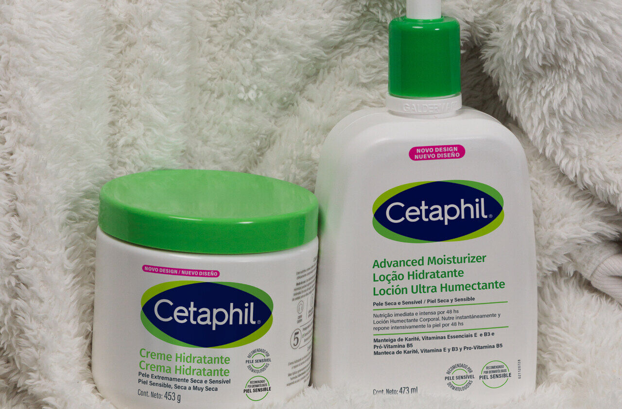 Dois produtos Cetaphil, um creme e uma loção, destacados em um fundo macio. Os rótulos indicam "Creme Hidratante" e "Advanced Moisturizer Loção Hidratante", com menção a "NOVO DESIGN".