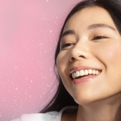 Mulher com pele iluminada em fundo rosa, representando o resultado de uma rotina de skincare coreana (K-beauty)