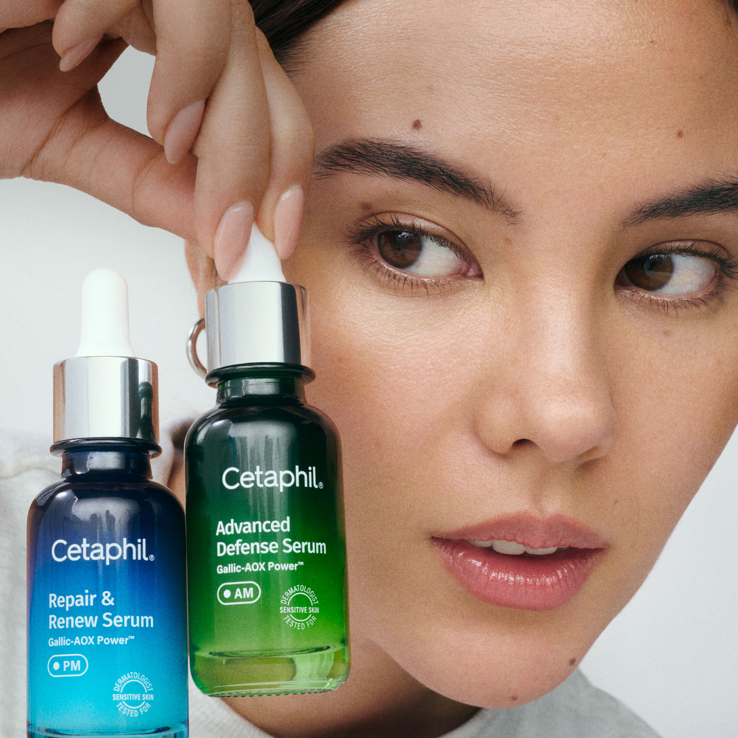 Close-up de uma mulher segurando dois frascos de s&eacute;rum Cetaphil ao lado do rosto; um frasco azul &ldquo;Repair & Renew Serum (PM)&rdquo; e um frasco verde &ldquo;Advanced Defense Serum (AM)&rdquo;.