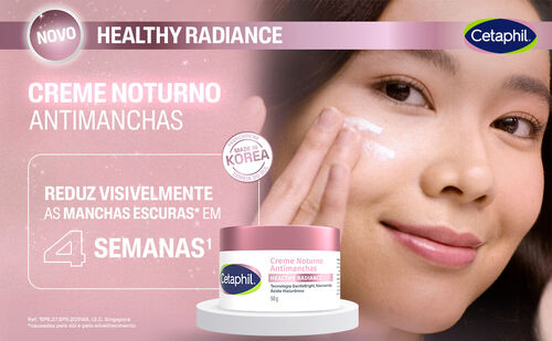 Uma mulher asiática com cabelo escuro e pele clara, com creme branco no rosto, olha para a câmera com um sorriso suave. Sua mão direita está levantada, aplicando o creme. No centro da imagem, um pote de creme noturno branco e rosa da Cetaphil está em destaque sobre um pedestal branco. O texto "NOVO HEALTHY RADIANCE" e "CREME NOTURNO ANTIMANCHAS" aparece na parte superior. Há também um selo "MADE IN KOREA" e a frase "REDUZ VISIVELMENTE AS MANCHAS ESCURAS EM 4 SEMANAS".