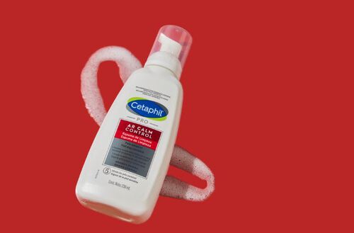 Frasco de Espuma de Limpeza Facial Cetaphil PRO AR Calm Control com espuma ao redor, sobre fundo vermelho.
