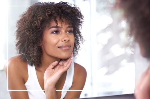 Mulher negra olhando para o espelho analisando sua pele.