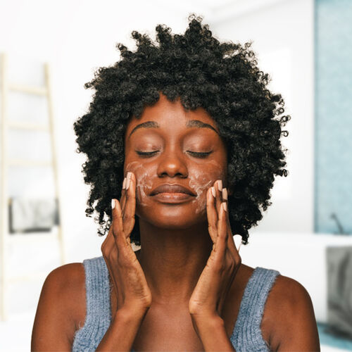 Mulher negra aplicando glicerina no rosto durante sua rotina de cuidados com a pele.