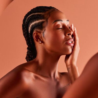 Mulher negra de olhos fechados e tocando a própria face