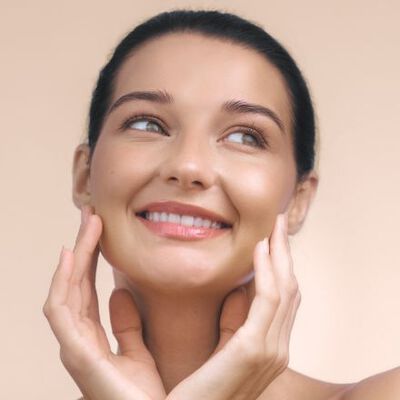 Mulher de pele branca sorrindo após aplicar creme com Vitamina E no rosto.