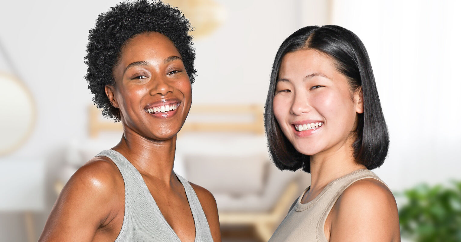 Mulher negra e mulher asi&aacute;tica com peles iluminadas e sorrindo.