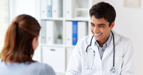 M&eacute;dico sorrindo atende paciente em consult&oacute;rio.