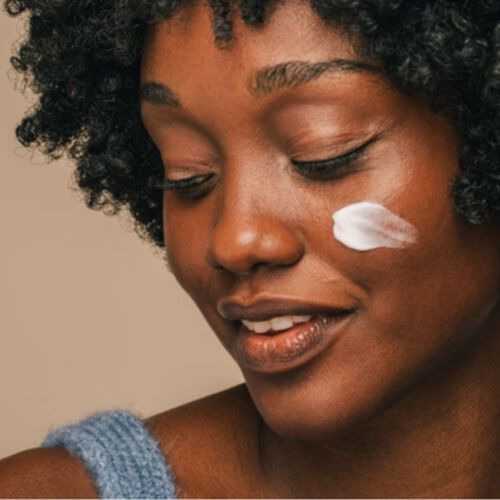 Mulher de pele negra com creme hidratante com niacinamida no rosto. 